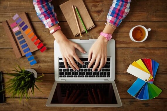 maos apoiadas sobum notebook com cartelas de cores, lápis e bloco