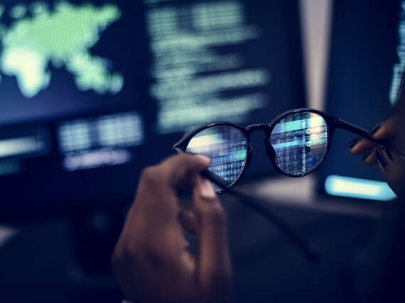 mão segurando oculos na frente de uma tela de computador, com vários números, simbolizando a A cultura do golpe no meio digital