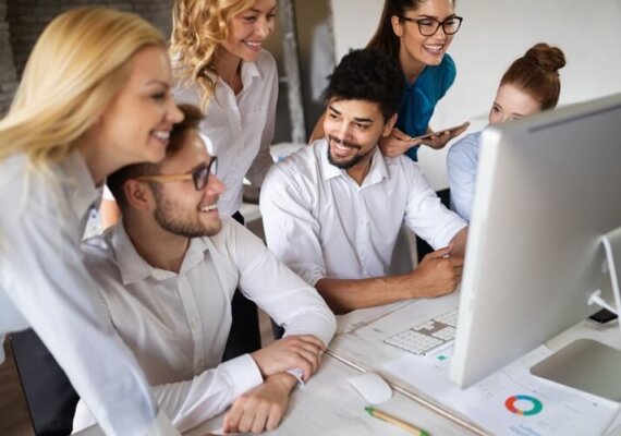 Cinco pessoas sorrindo olhando a tela de um computador, representando o blogpost sobre como inspirar seus funcionários nas redes sociais.