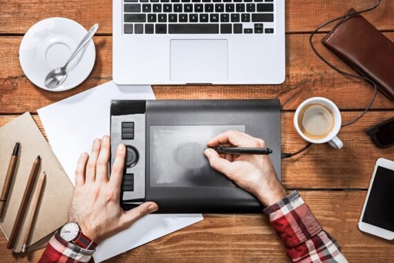 designer criando uma peça em equipamento na frente de um compuatdor, com uma xícara ao lado