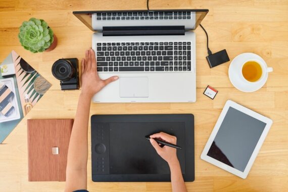 Designer desenhando o projeto, com uma mão no notebook e outra na mesa