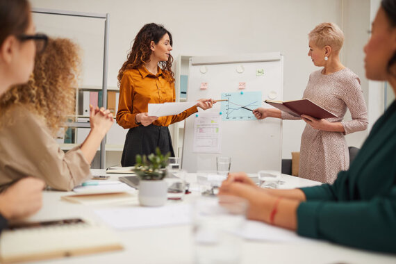 Duas mulheres fazendo uma apresentação, mostrando dados sobre como fazer um pitch de sucesso.