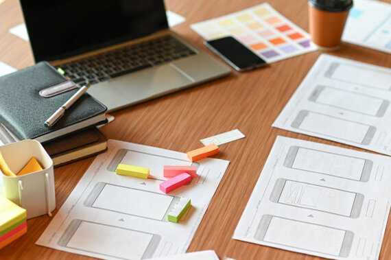 como resolver problemas com workshops de design: Imagem de um computador com vários papéis, canetas e post-its em uma mesa