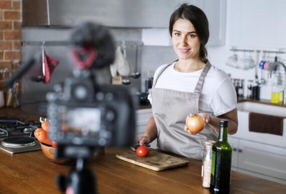 Como fazer uma boa live: mulher na cozinha, segurando uma cebola em direção a uma câmera no tripé