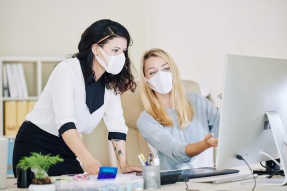 Duas mulheres de máscaras na frente de um computador