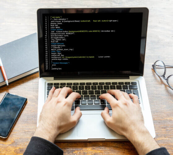 uma mesa com computador e as mãos de usa pessoa programando algo na tela.