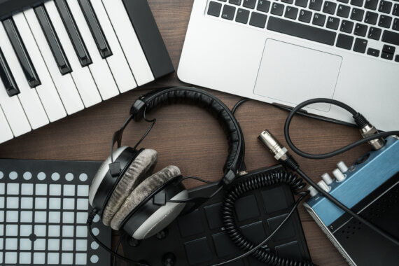 Mesa com computado, teclado e fone de ouvido, indicando a produção de uma identidade sonora de marca.