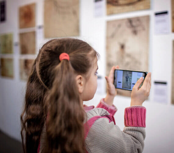 menina tendo uma experiência que mistura digital e real em um museu olhando o celular
