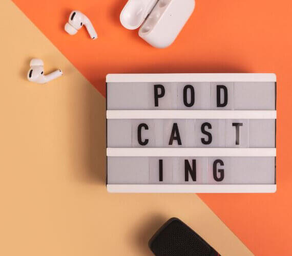 Letreiro com a palavra podcasting, microfones e fones de ouvido em volta e fundo laranja